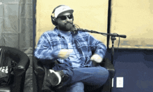 a man in a plaid shirt is sitting in front of a microphone wearing headphones and sunglasses