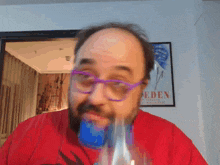 a man wearing glasses and a red shirt stands in front of an eden poster