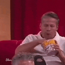 a man is sitting on a red couch eating a bag of chips .
