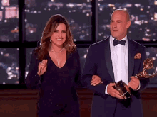 a man in a tuxedo holds a trophy next to a woman in a dress