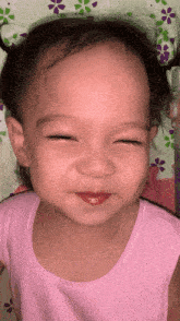a little girl wearing a pink tank top is smiling with her eyes closed