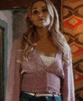 a woman is wearing a purple cardigan and jeans and standing in a room .