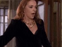 a woman in a black dress and gold necklace is standing in a hallway with her mouth open .