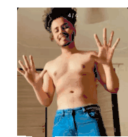 a shirtless man in blue jeans is standing in front of a mirror and waving his hands .