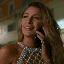 a woman wearing a pearl necklace is talking on her phone