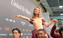 a woman in a red dress is being lifted by a man in front of a wall that says united by music
