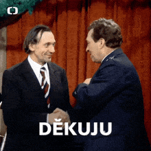 two men shaking hands in front of a red curtain and a sign that says dekuji