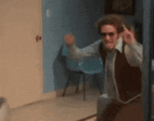 a man wearing sunglasses and a vest is standing in a hallway .