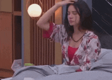 a woman is sitting on a bed with her eyes closed and scratching her head .