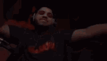 a man wearing headphones and a t-shirt is dancing in a dark room with his arms outstretched .
