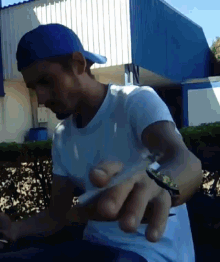 a man wearing a white shirt and a blue hat holds a cigarette in his hand