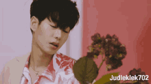 a man in a red and white shirt is holding a flower and the name judleklek702 is on the bottom right