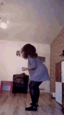 a woman is dancing in a living room with a brick wall behind her