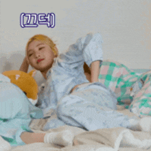a woman in pajamas is laying on a bed with a stuffed animal behind her