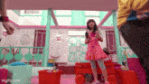 a girl in a pink dress is standing next to a red wagon in front of a pink house .
