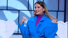 a woman wearing a blue coat and purple turtleneck is standing in front of two hearts