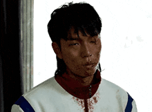 a man with blood on his face is wearing a white jacket with blue and red stripes