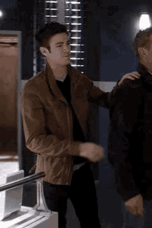 a man in a brown jacket is standing next to another man in a dark room .