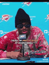 a man wearing sunglasses and a beanie is sitting in front of a microphone and talking about basketball