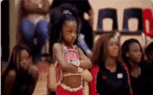 a girl in a cheerleader outfit is standing with her arms crossed in front of a crowd of people .