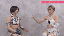 two female wrestlers are sitting next to each other and one is pointing at the other