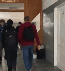a man wearing a nike backpack walks down a hallway with others