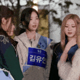 a girl wearing a blue vest with s5 on it talks to two other girls