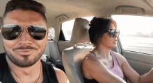 a man and a woman are sitting in a car and the woman is wearing sunglasses