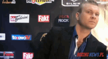 a man in a suit stands in front of a wall with boxing news.pl written on it
