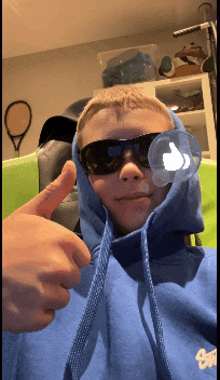 a boy wearing sunglasses and a blue hoodie giving a thumbs up
