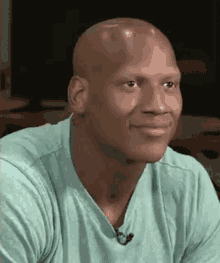 a bald man wearing a green shirt with a microphone on it is smiling .