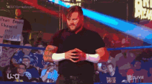 a man in a blue shirt stands in a wrestling ring with a usa logo on the bottom right