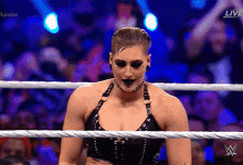 a woman in a black top is standing in a wrestling ring with a crowd watching .