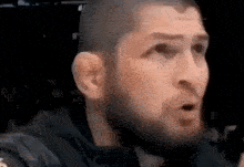 a man with a beard is talking into a microphone with his mouth open .