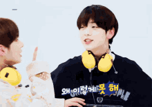 a boy wearing headphones talks to another boy with korean writing on it