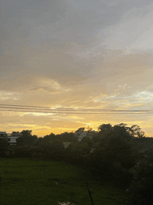 a sunset over a lush green field with a few buildings in the background