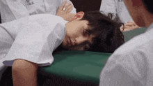 a boy in a white shirt is laying on a green table with his eyes closed .