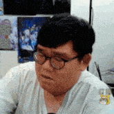 a man wearing glasses and a white shirt is sitting in front of a wall with posters on it