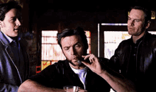 a man is smoking a cigarette and drinking a glass of whiskey while another man looks on .