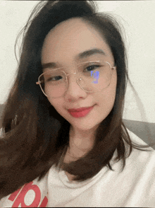 a woman wearing glasses and a white shirt with the letter b on it smiles for the camera