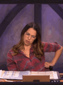 a woman wearing glasses is sitting at a desk with binders and a laptop