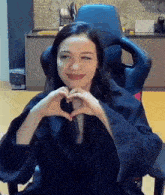 a woman is sitting in a gaming chair making a heart shape with her hands .