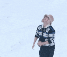 a person wearing a hat and a sweater is standing in the snow and looking up