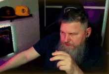 a man with a beard is sitting in front of a computer and making a funny face .