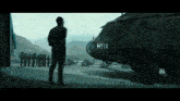 a man stands in front of a helicopter with the numbers h114 on the side