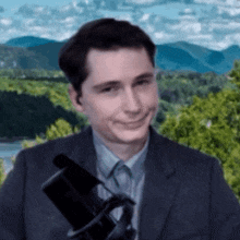 a man in a suit and tie holds a microphone in front of a mountain range