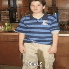 a young boy in a striped shirt and khaki pants is standing in a kitchen with a wet spot on his pants .