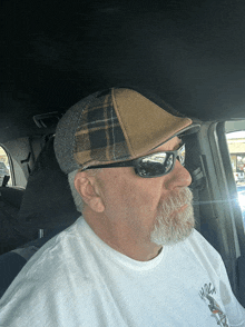 a man wearing sunglasses and a plaid hat is sitting in a car