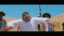 a man in a white shirt and a head scarf is holding a gun in the desert .