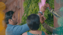 two men are holding pink cotton candy in front of a wall of green leaves